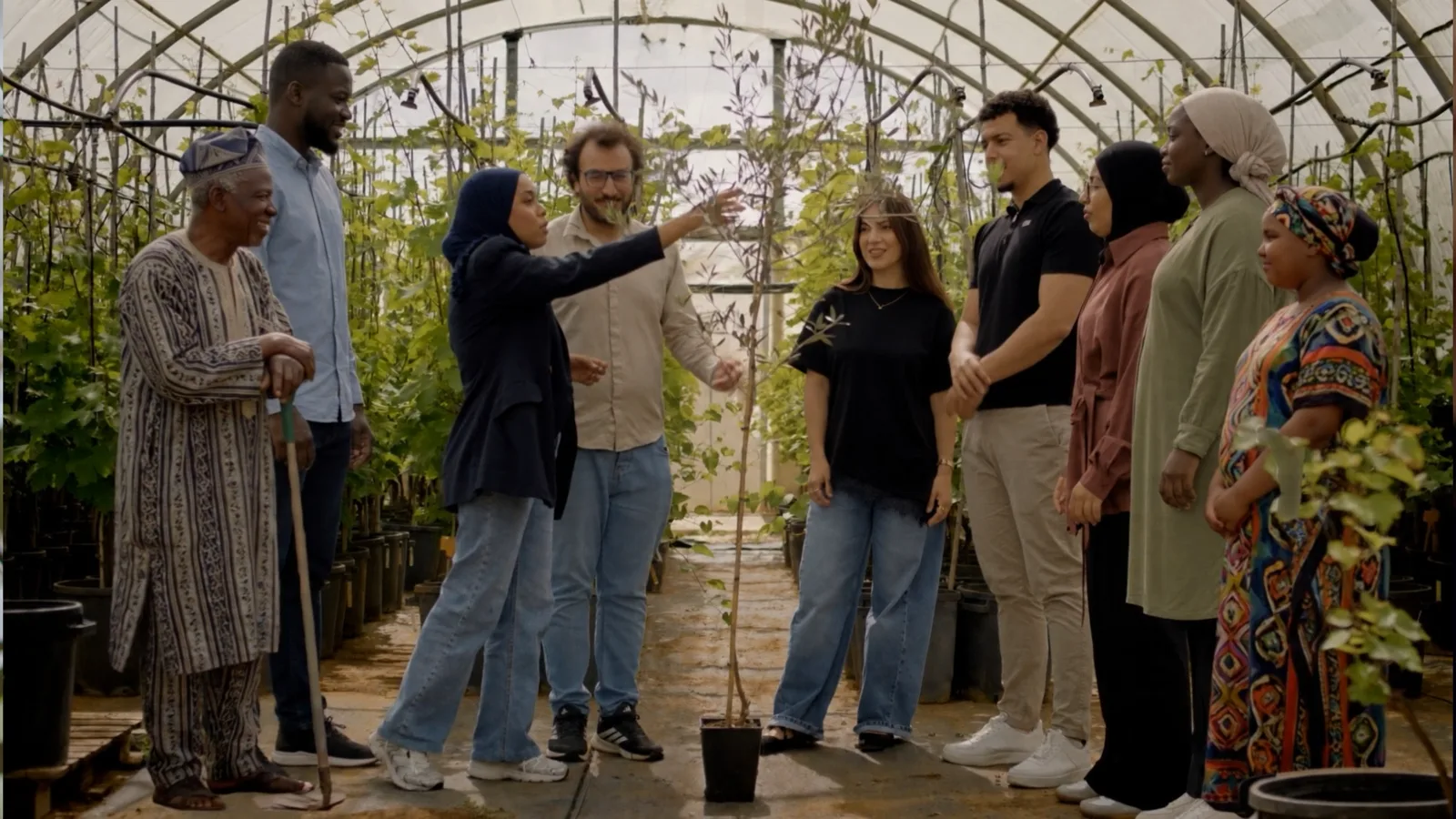 Un gruppo di persone di diverse generazioni in serra attorno a un giovane albero